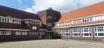 De achterzijde van het L-vormige gebouw, met het schoolplein.
              <br/>
              Joop de Haan, 2023