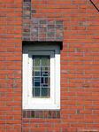 Raampje met glas-in-lood op de verdieping, geaccentueerd door contrasterende bakstenen.
<br/>
Gert-Jan Lobbes, 2022