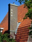 De (verlaagde en vereenvoudigde) schoorsteen bevat de naam van het huis.
<br/>
Gert-Jan Lobbes, 2025
